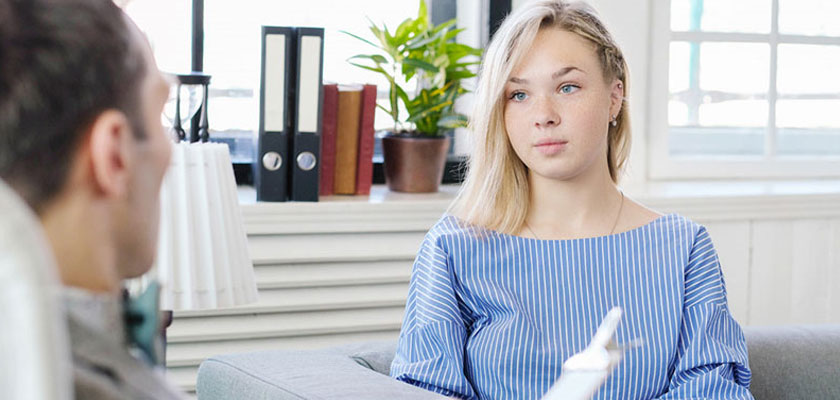 ζωγραφιά που απεικονίζει μια θεραπεύτρια και μια θεραπευόμενη με τη τσάντα της θεραπεύτριας να έχει ανοίξει και να προβάλλει προσωπικά αντικείμενα